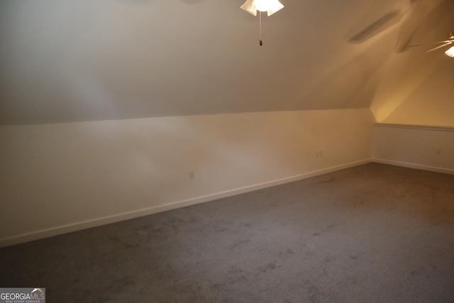 additional living space featuring vaulted ceiling, dark carpet, a ceiling fan, and baseboards