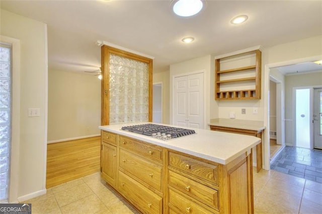 kitchen featuring a center island, stainless steel gas cooktop, open shelves, light countertops, and baseboards