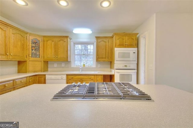 kitchen featuring recessed lighting, light countertops, glass insert cabinets, a sink, and white appliances