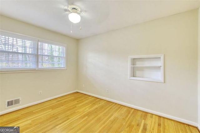 spare room with wood finished floors, visible vents, and baseboards