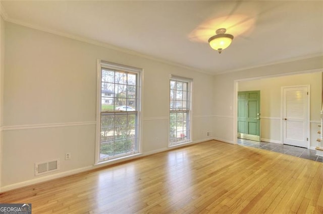 spare room with ornamental molding, visible vents, baseboards, and wood finished floors