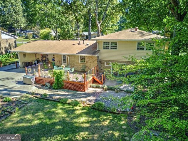 rear view of house with driveway, brick siding, a lawn, and a wooden deck