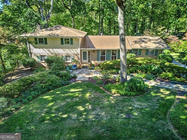 split level home with a patio area, brick siding, a chimney, and a front lawn