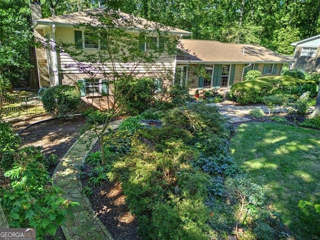 tri-level home with brick siding, a chimney, a front lawn, and fence