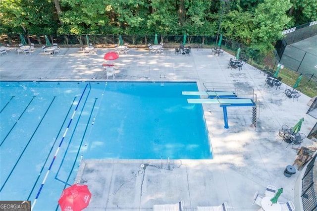 pool featuring a diving board, a patio area, and fence