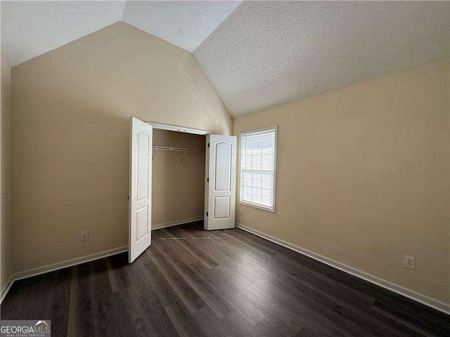 unfurnished bedroom with baseboards, dark wood-style floors, vaulted ceiling, a textured ceiling, and a closet