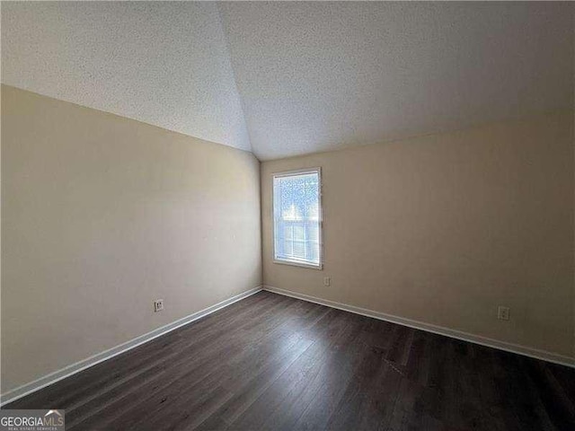 empty room with dark wood-style floors, a textured ceiling, lofted ceiling, and baseboards