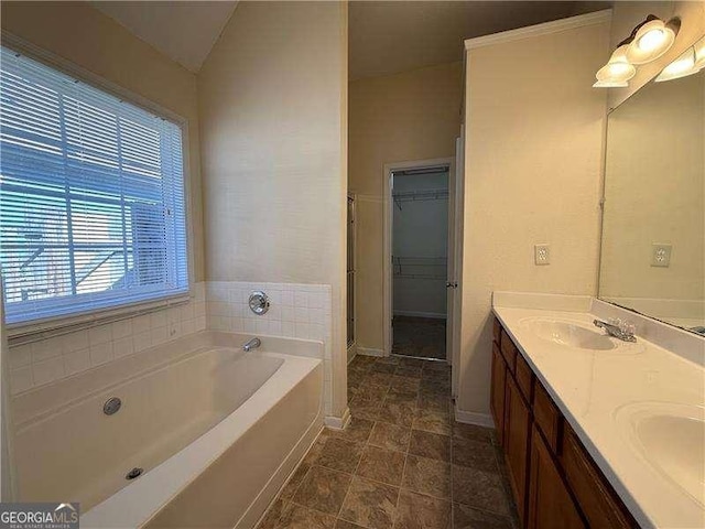 full bathroom with a garden tub, double vanity, a spacious closet, a sink, and baseboards