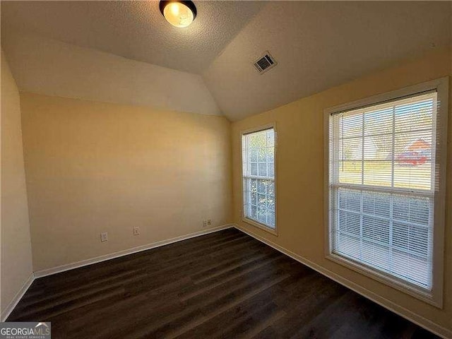 unfurnished room with baseboards, visible vents, dark wood-type flooring, vaulted ceiling, and a textured ceiling