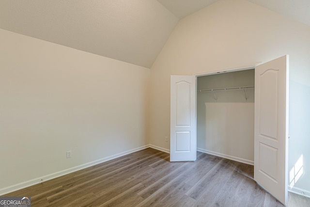 unfurnished bedroom featuring lofted ceiling, baseboards, wood finished floors, and a closet