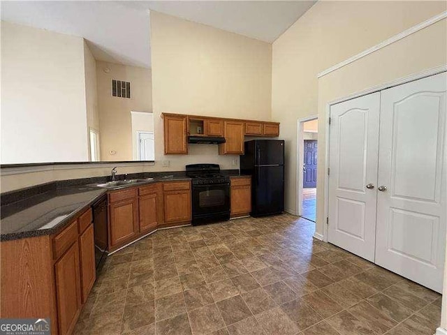 kitchen with brown cabinetry, dark countertops, under cabinet range hood, and black appliances