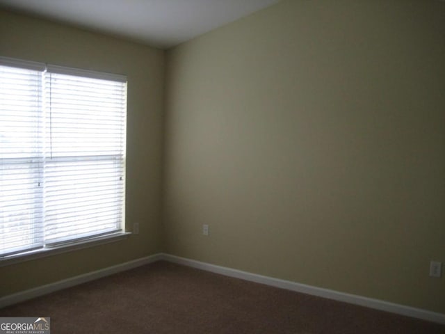 unfurnished room with dark colored carpet and baseboards