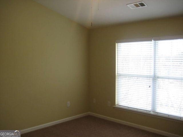 spare room with dark colored carpet, visible vents, and baseboards