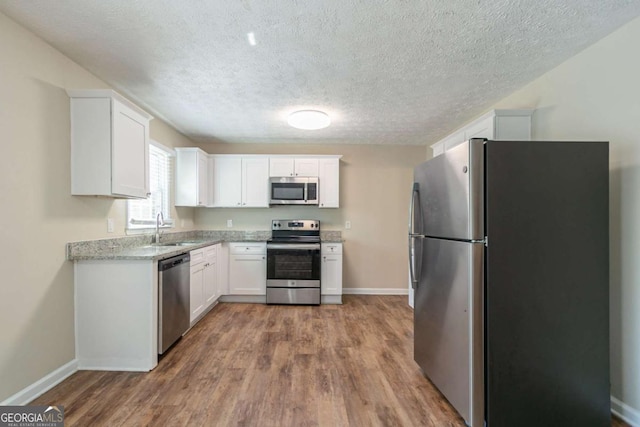 kitchen featuring appliances with stainless steel finishes, white cabinets, a sink, and wood finished floors