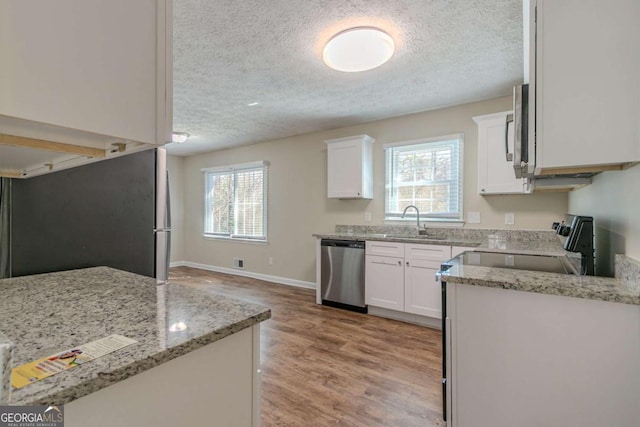 kitchen featuring light wood-style flooring, stainless steel appliances, a sink, white cabinets, and plenty of natural light