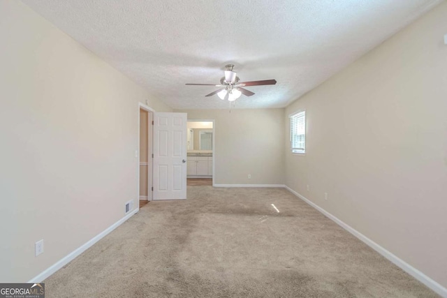 spare room featuring a textured ceiling, ceiling fan, light colored carpet, visible vents, and baseboards