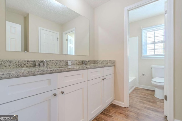 bathroom with toilet, a sink, a textured ceiling, and wood finished floors