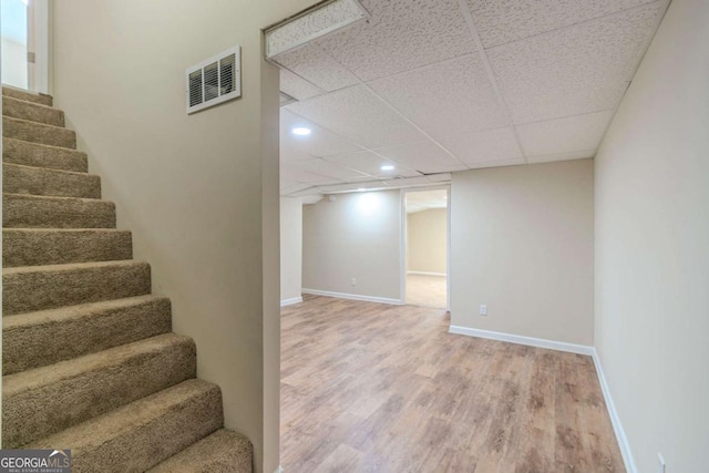 finished below grade area with visible vents, stairway, baseboards, and wood finished floors