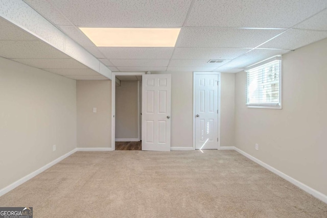 below grade area featuring carpet floors, a drop ceiling, visible vents, and baseboards