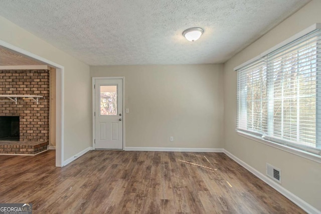 entryway with baseboards, visible vents, wood finished floors, a textured ceiling, and a fireplace