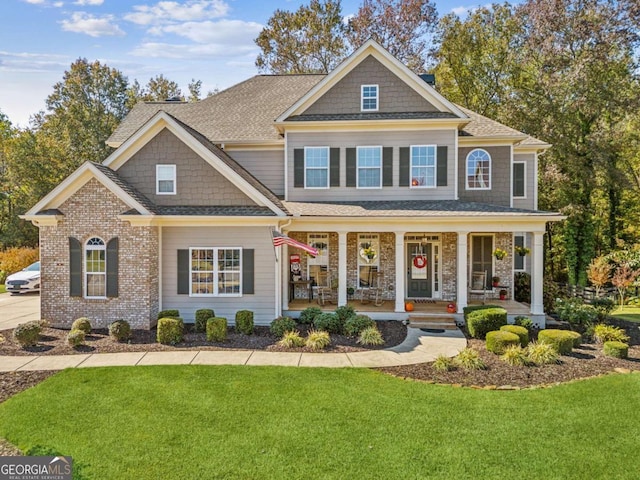 view of front of house with brick siding, covered porch, a front yard, and roof with shingles