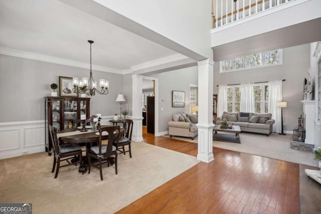 dining room featuring an inviting chandelier, crown molding, light wood-type flooring, and ornate columns