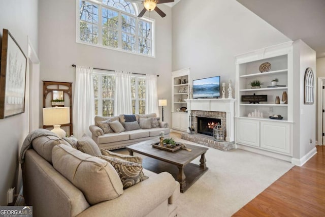 living room with plenty of natural light, a brick fireplace, wood finished floors, and a ceiling fan