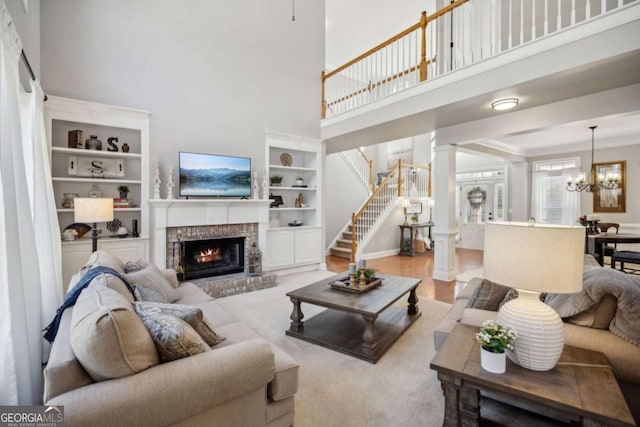 living room with a chandelier, stairway, built in features, decorative columns, and a fireplace