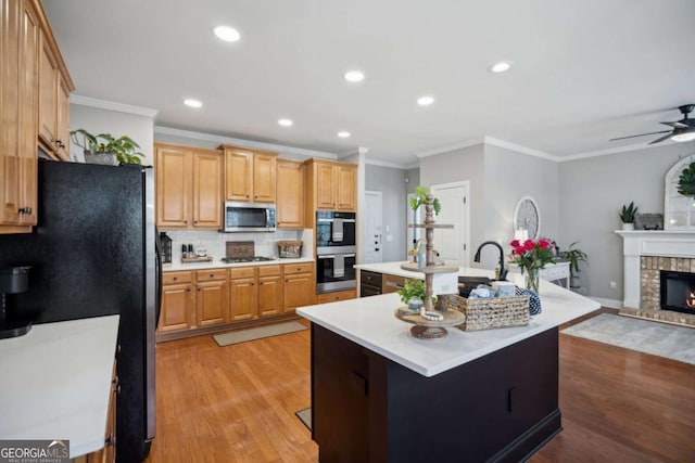 kitchen with a fireplace, a kitchen island with sink, stainless steel appliances, light countertops, and light wood-style floors