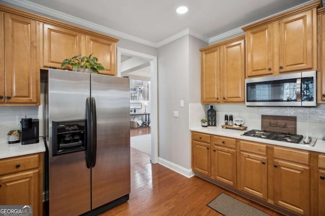 kitchen featuring appliances with stainless steel finishes, wood finished floors, crown molding, and light countertops