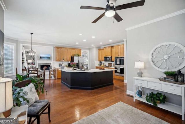 living room featuring ornamental molding, ceiling fan with notable chandelier, a warm lit fireplace, wood finished floors, and recessed lighting