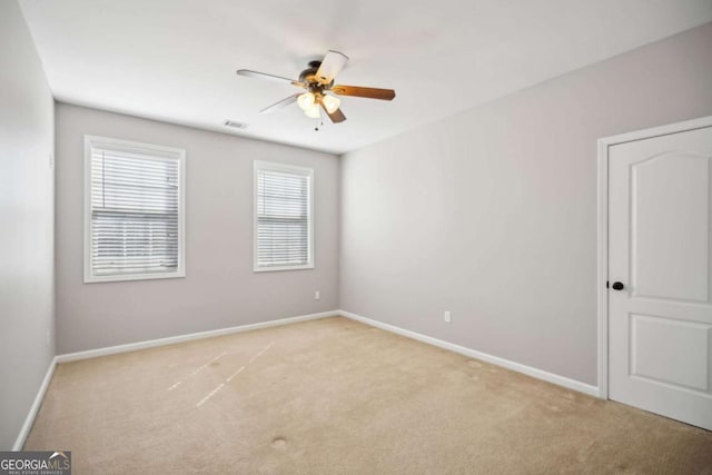 empty room featuring a ceiling fan, visible vents, light colored carpet, and baseboards