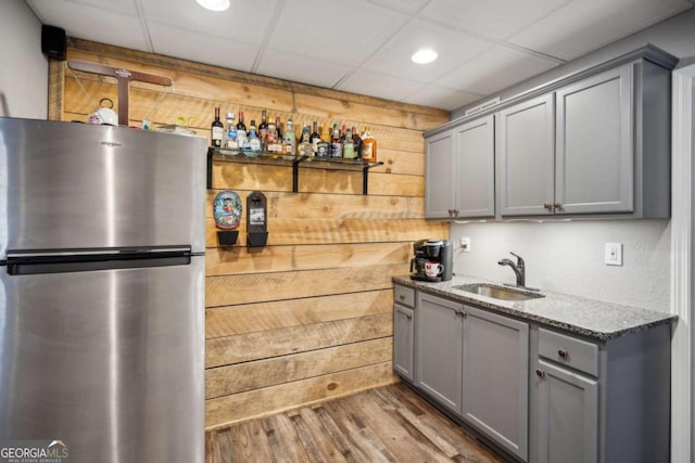 kitchen featuring a sink, gray cabinetry, wood walls, and freestanding refrigerator