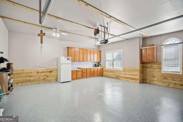 garage with a wainscoted wall, wood walls, a garage door opener, and freestanding refrigerator