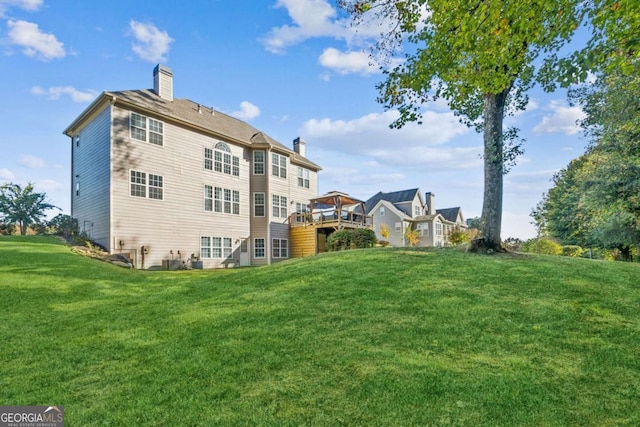 rear view of house featuring a wooden deck, a lawn, and a chimney