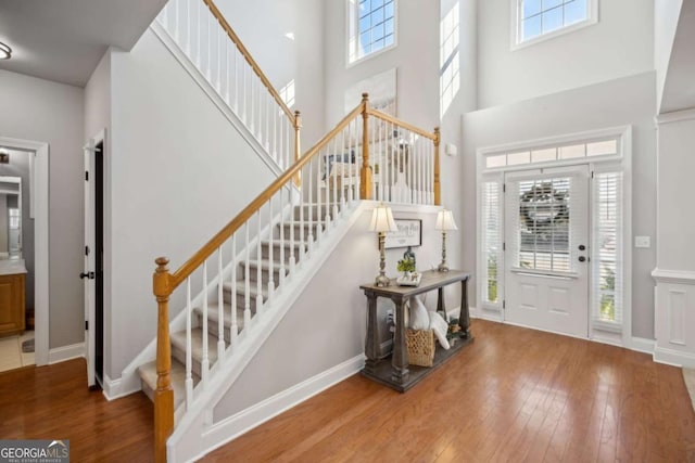 foyer entrance with a healthy amount of sunlight, a towering ceiling, stairs, and hardwood / wood-style flooring