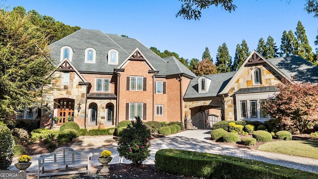 french provincial home with driveway, a gate, stone siding, a garage, and brick siding