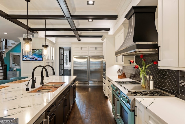 kitchen featuring a sink, premium appliances, coffered ceiling, white cabinetry, and wall chimney range hood