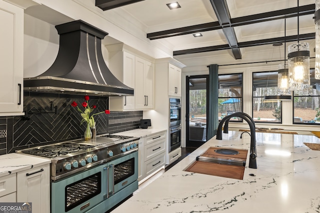 kitchen with beamed ceiling, coffered ceiling, white cabinets, wall chimney range hood, and range with two ovens