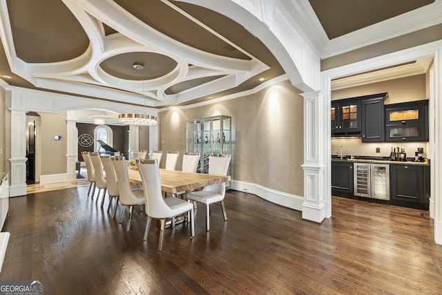 dining area featuring beverage cooler, decorative columns, ornamental molding, dark wood-type flooring, and bar