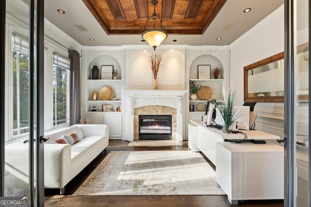 living room featuring built in shelves, a raised ceiling, ornamental molding, and a fireplace