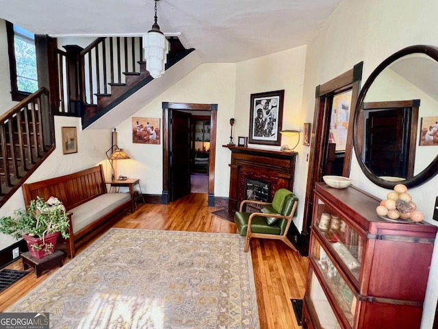 living area featuring a fireplace with flush hearth, stairs, baseboards, and wood finished floors