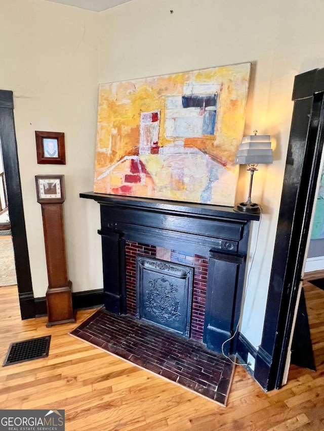 details with a brick fireplace, wood finished floors, visible vents, and baseboards