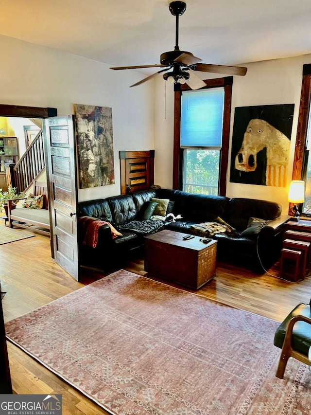 living area with ceiling fan, stairway, and wood finished floors