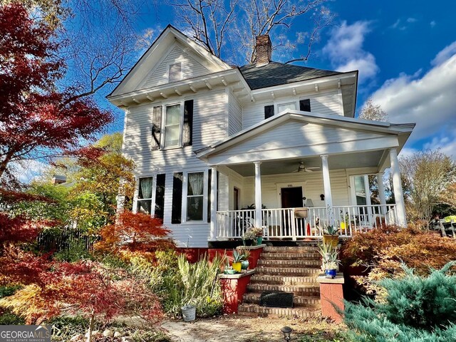 victorian house with a chimney, a porch, and a ceiling fan