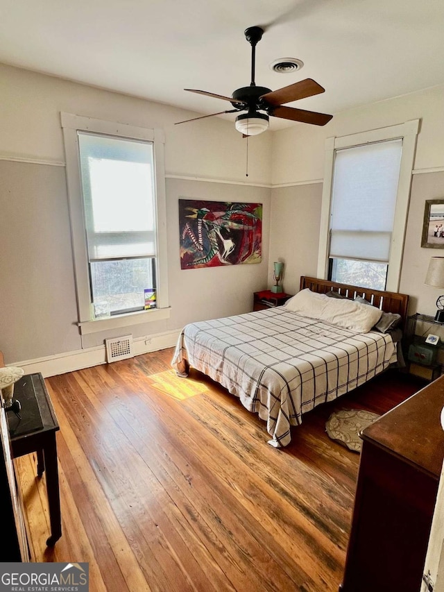 bedroom with ceiling fan, wood finished floors, visible vents, and baseboards