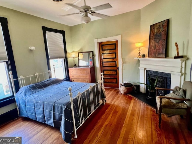 bedroom featuring wood-type flooring, a ceiling fan, and a high end fireplace