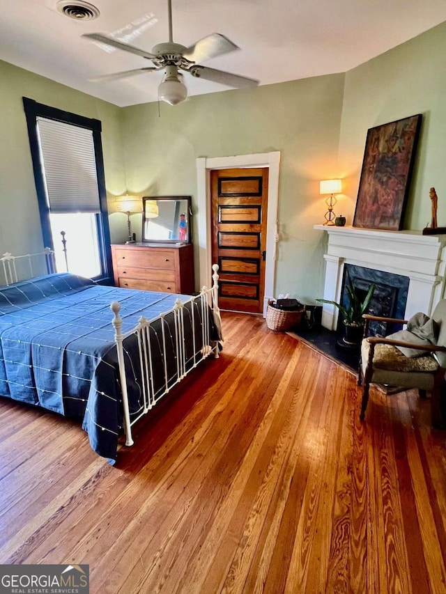 bedroom featuring ceiling fan, a premium fireplace, visible vents, and hardwood / wood-style floors