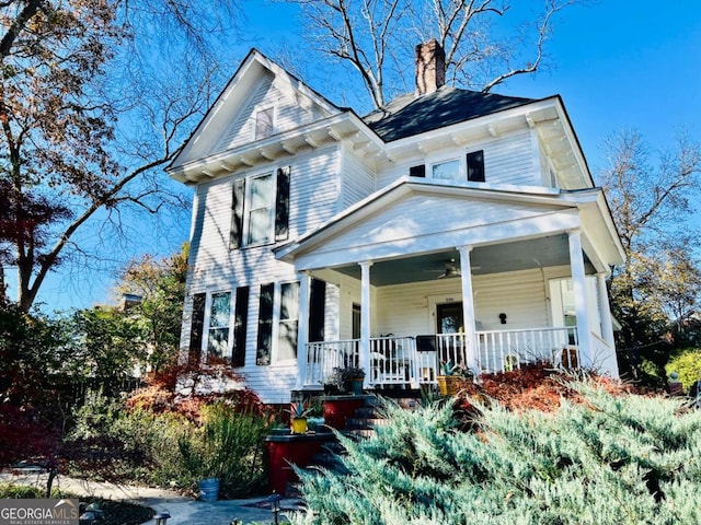 view of front of house featuring covered porch, ceiling fan, and a chimney