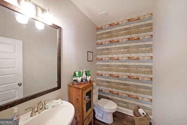 half bathroom featuring visible vents, wooden walls, baseboards, toilet, and a sink